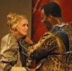 Othello has his hands around Desdemona's neck as she cries looking up at him. Both are dressed in ornate gold and black Renaissance outfits